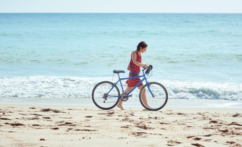 woman walking on the beach with a bicycle